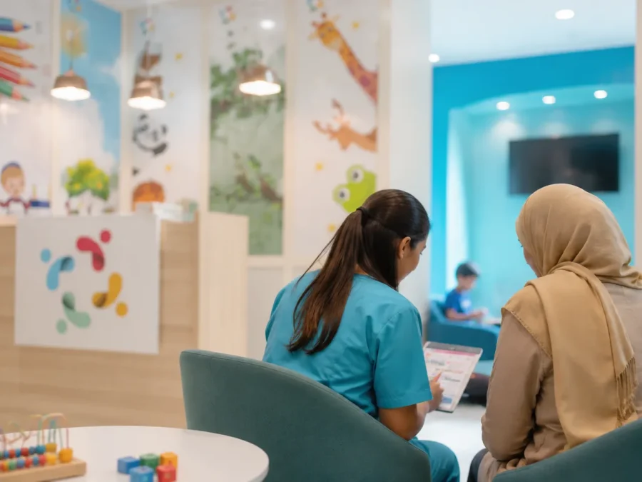 Une soignante en tunique turquoise présente un document sur tablette à une mère assise à ses côtés, dans l’espace d’accueil du centre