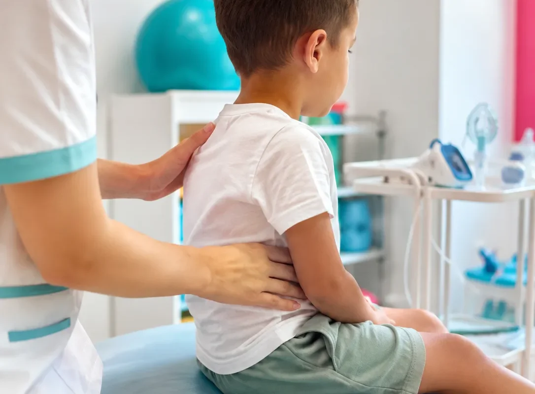 Une kinésithérapeute réalise une manœuvre de kinésithérapie respiratoire sur un garçon assis sur la table de soins