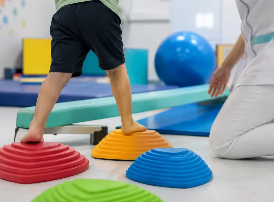 Un garçon franchit en équilibre un parcours de plots colorés, guidé par une soignante dans la salle de psychomotricité